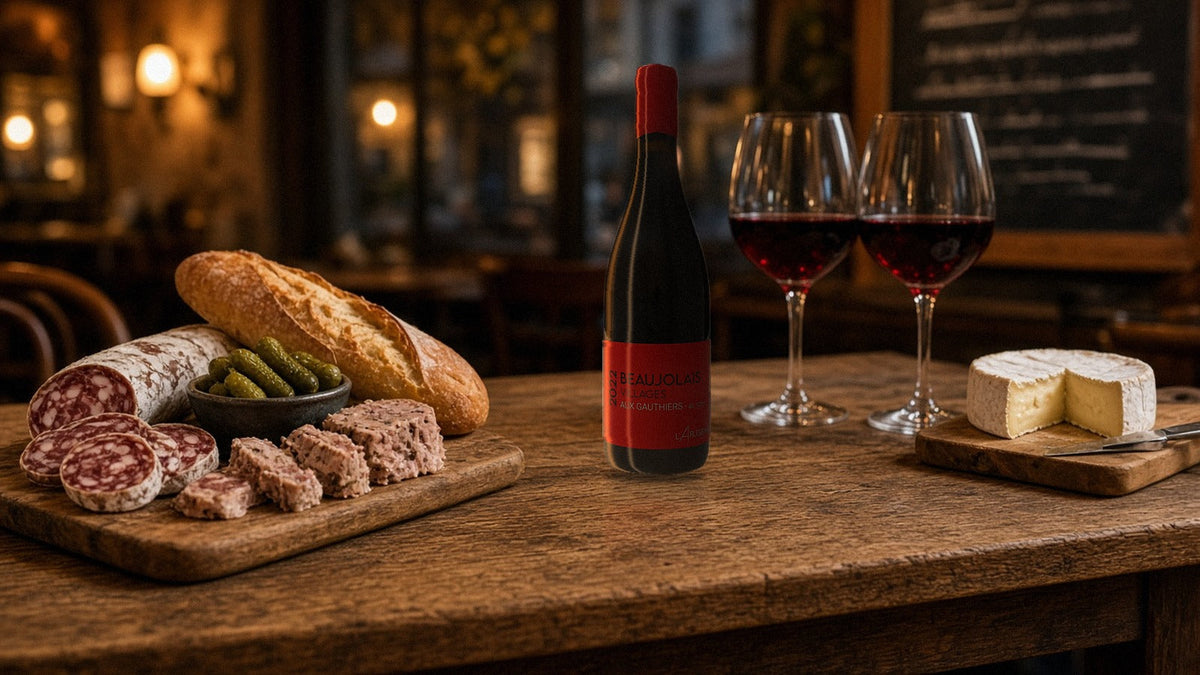 Bottle of L'Arlésienne Beaujolais-Villages Aux Gauthiers 2022 on a bistro table with charcuterie, cheese and two glasses of red wine